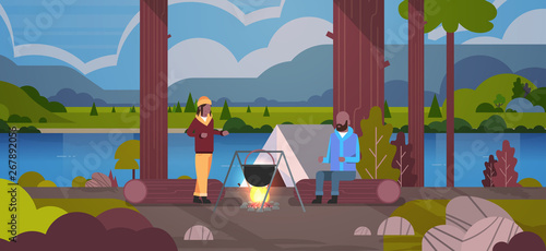 african american couple hikers man woman cooking meals in bowler boiling pot at campfire near camp tent camping concept landscape nature river mountains background horizontal full length