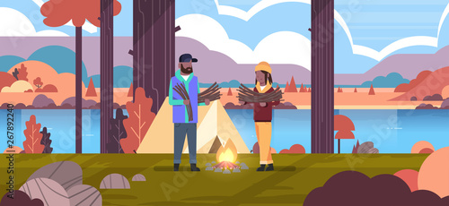 couple tourists hikers holding firewood african american man woman organizing fire n camp tent hiking camping concept autumn landscape nature river mountains background horizontal full length