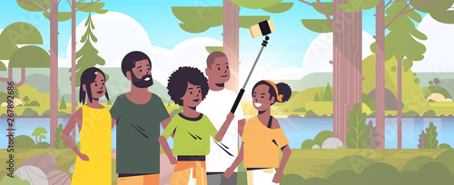 people group in forest using selfie stick taking photo on smartphone camera hiking concept african american friends standing together landscape background portrait horizontal