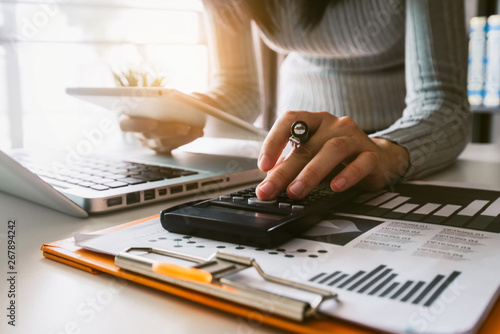 Businesswoman hands working with finances about cost and calculator and laptop with tablet, smartphone at office in morning light