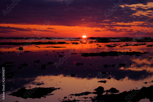 Beautiful red sunset. The sun is setting in the sea. Reflection in the sea, rocky shore. Sun rays. © taisiyakozorez