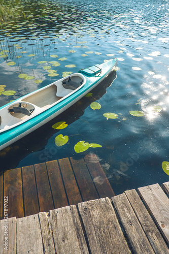 Fototapeta Naklejka Na Ścianę i Meble -  Zielony dwuosobowy kajak przycumowany przy drewnianym pomoście, dookoła unoszą się lilie