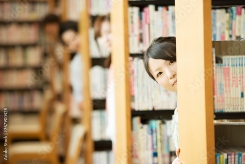 図書館の本棚から顔を出す大学生