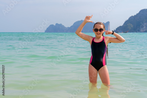 Beautiful girl in a black bathing suit on the sea on a sunny day. Happy child in glasses on the ocean with copy space. Concept of sunny and happy summer.