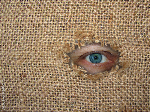 The man's eye looks through a hole in the torn sack. Burlap background.