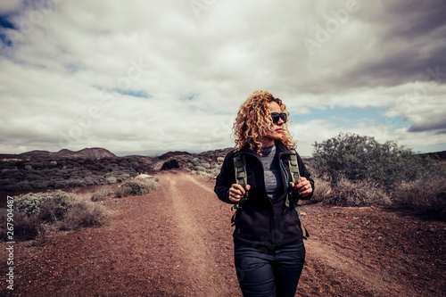 Beautiful trekker caucasian blonde curly young active woman walk in the desert path enjoying the freedom and the active lifestyle traveling with backpack alone in the outdoors natural park photo