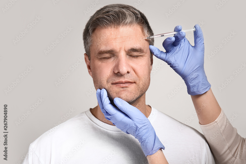 Mature man and hands holding syringe for anti-aging injections on grey background Mature man and hands holding syringe for anti-aging injections on grey background
