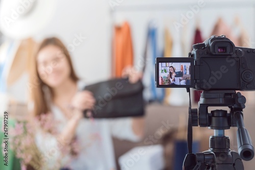 Beautiful asian woman blogger is showing shopping clothes and bag. In front of the camera to recording vlog video live streaming at home.Business online influencer on social media concept. photo
