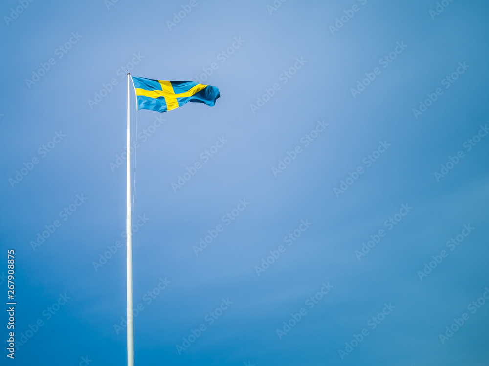 Swedish flag against blue sky. Swedish flag fluttering on wind. Sveriges nationaldag. National Day of Sweden. Swedish Flag Day. Swedish flag against blue sky. Swedish flag fluttering on wind. Sveriges nationaldag. National Day of Sweden. Swedish Flag Day.