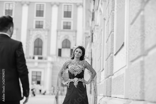 Canvas Print Beautiful woman in a long red dress walks around the city with her husband in a