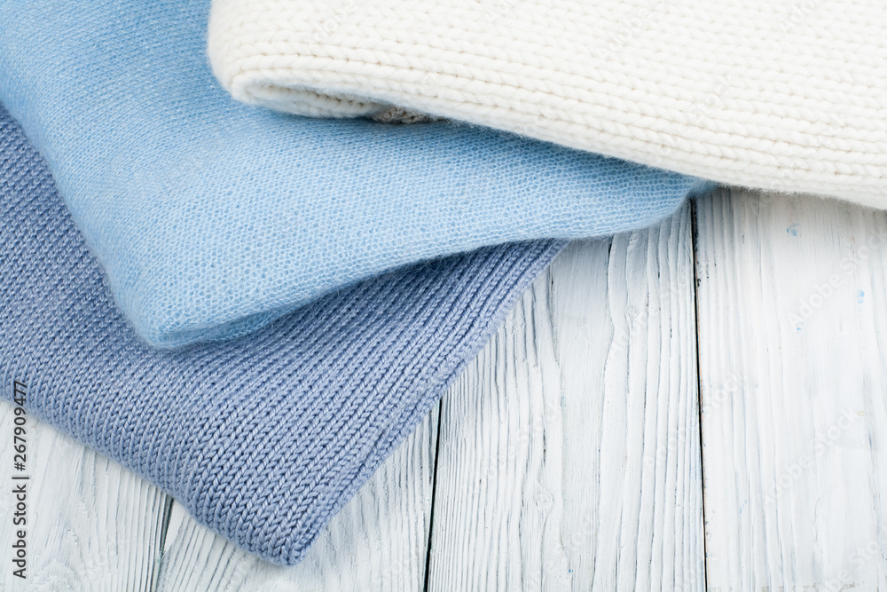 Knitted wool sweaters. Pile of knitted winter clothes on wooden background, sweaters, knitwear, space for text. Knitted wool sweaters. Pile of knitted winter clothes on wooden background, sweaters, knitwear, space for text.