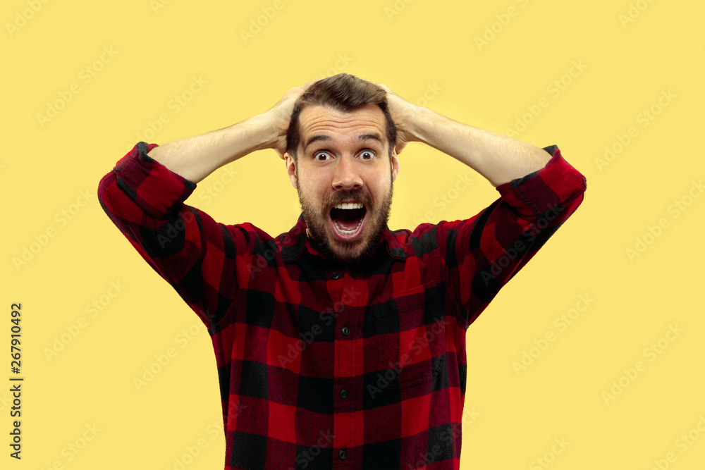 Half-length close up portrait of young man in shirt on yellow background. The human emotions, facial expression concept. Trendy colors. Astonished and crazy screaming while holding his head. Half-length close up portrait of young man in shirt on yellow background. The human emotions, facial expression concept. Trendy colors. Astonished and crazy screaming while holding his head.