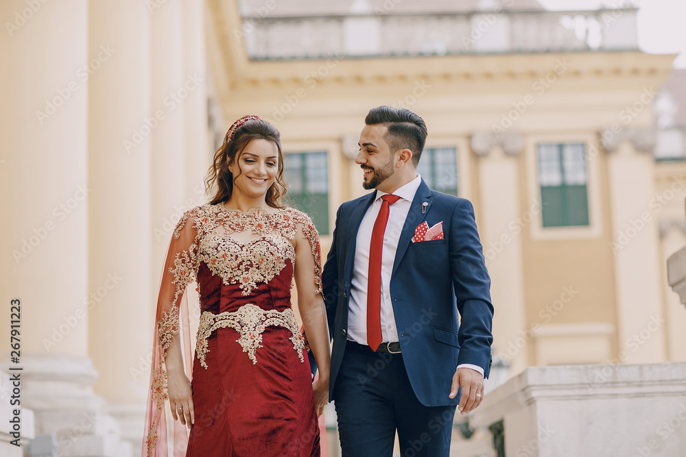 Beautiful woman in a long red dress walks around the city with her husband in a blue suit and with a beard Beautiful woman in a long red dress walks around the city with her husband in a blue suit and with a beard
