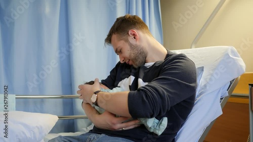 Happy father holds his newborn baby daughter in maternity hospital room photo