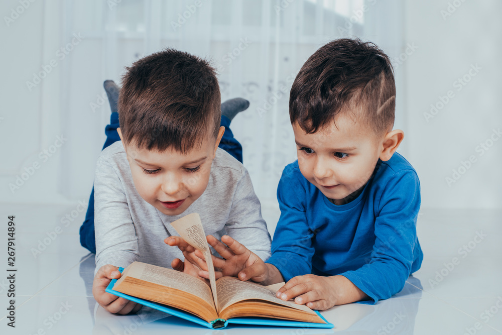 Photo of two charming boys, brothers or friends, lying on the floor smiling happily reading a book. Photo of two charming boys, brothers or friends, lying on the floor smiling happily reading a book.