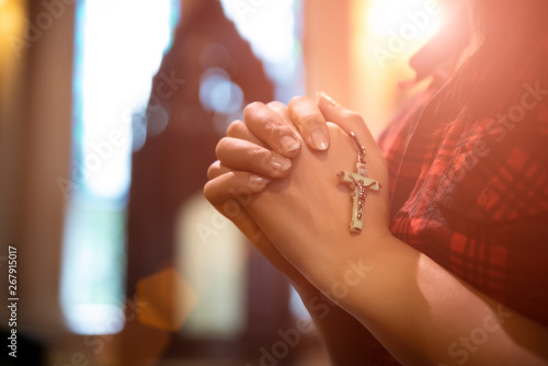 Woman hand holding rosary against cross and praying to God at church.