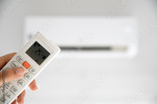 woman hand holding remote controller directed on the air conditioner inside the room and set at ambient temperature,25 degrees celsius.