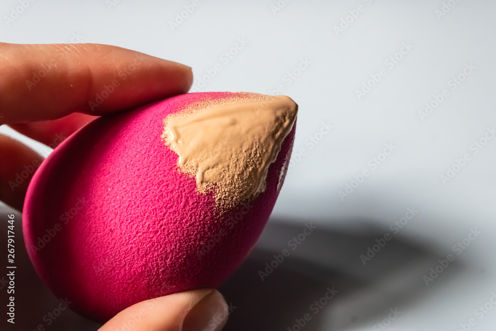 Woman hand holding pink beauty blender with the beige liquid foundation on  it - Image Stock-Foto | Adobe Stock