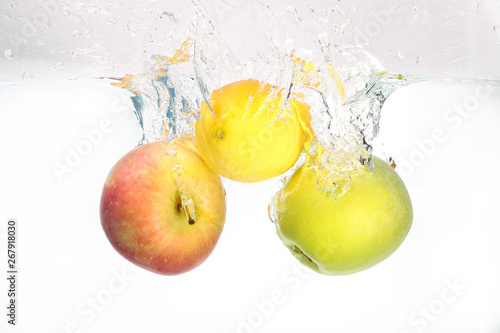 Two apples and lemon splash in water on white