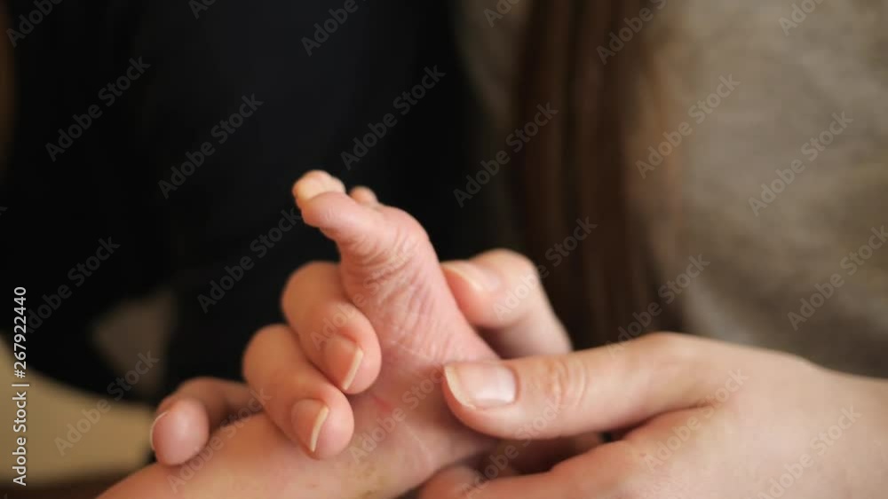 Tender mother fingers making massage to newborn baby small foot care in maternity hospital couple of days after birth