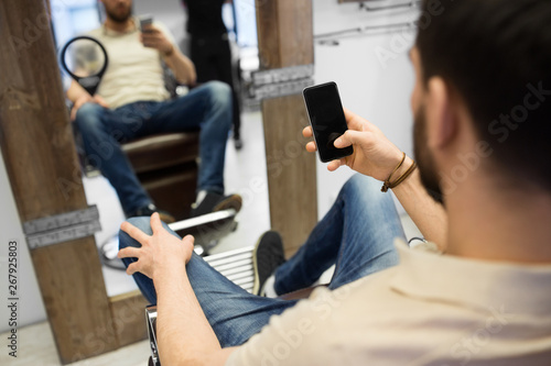 grooming  technology and people concept - man with smartphone at barbershop or hair salon