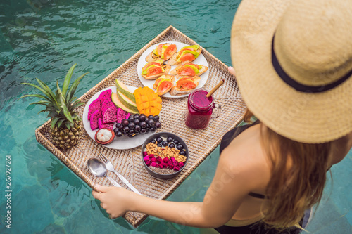 Breakfast tray in swimming pool, floating breakfast in luxury hotel. Girl relaxing in the pool drinking smoothies and eating fruit plate, smoothie bowl by the hotel pool. Exotic summer diet. Tropical photo