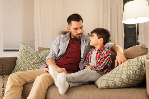 family, relationships and trust concept - father talking to his sad little son at home in evening photo