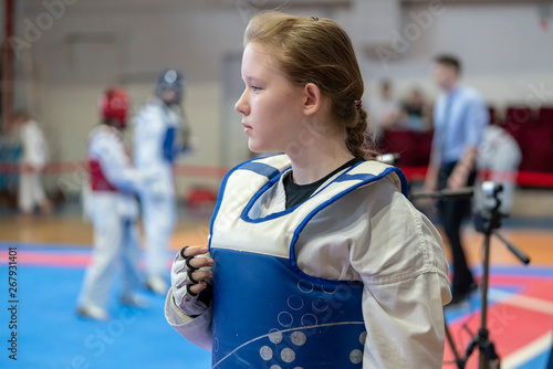 a girl participating in Taekwondo competitions in a blue protective vest on the background of Taekwondo competitions close-up