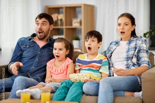 family, leisure and people concept - scared or surprised mother, father, son and daughter with popcorn watching horror on tv at home