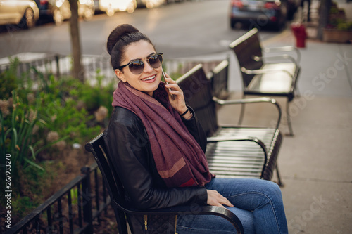 beautiful young girl in a leather jacket and scarf sitting on the streets of Chicago in the beautiful weather with phone © prostooleh