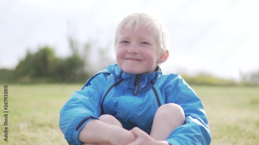 A handsome albino boy sitting in a park on the grass and smiling. Happy child on a spring walk in Cyprus. The child in the rain sits on the grass and smiles. Close-up of a happy blond boy A handsome albino boy sitting in a park on the grass and smiling. Happy child on a spring walk in Cyprus. The child in the rain sits on the grass and smiles. Close-up of a happy blond boy