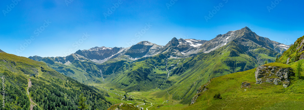 Panorama einer Bergkette mit saftigen Wiesen und massiven Felsen im idyllischen Salzburger Land unter blauem Himmel.