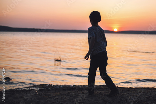 boy at sunset on the beach throws stones into the water