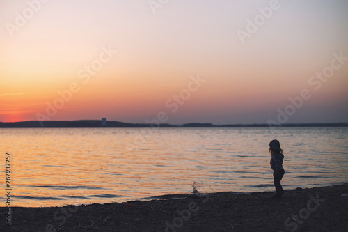 little girl at sunset on the beach throws stones into the water