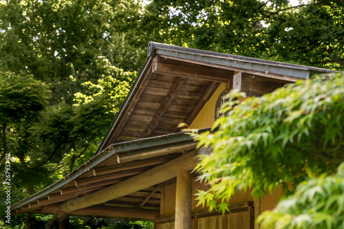Upper part of a small Japanese teahouse in a garden covered with dense trees © Frank