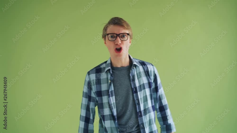 Portrait of angry young man shouting and looking at camera standing alone on green background expressing anger and irritation. Human emotions concept. Portrait of angry young man shouting and looking at camera standing alone on green background expressing anger and irritation. Human emotions concept.
