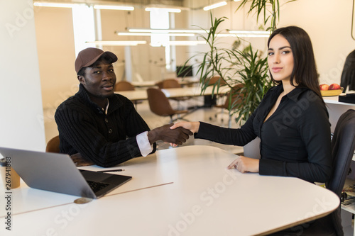 Confident caucasian woman shaking hands with african co-worker at desk in agreement