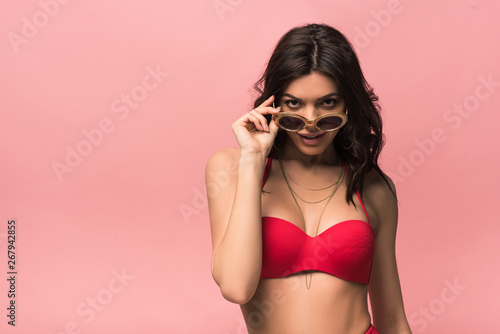 front view of smiling attractive woman in swimsuit and sunglasses isolated on pink