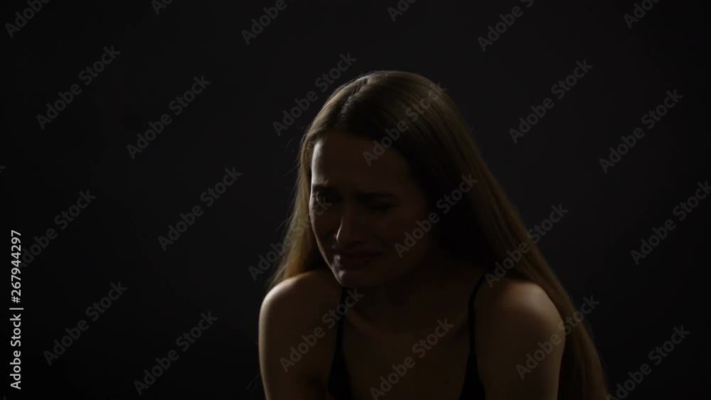 Crying lady sitting alone against dark background, suffering from life problems Crying lady sitting alone against dark background, suffering from life problems