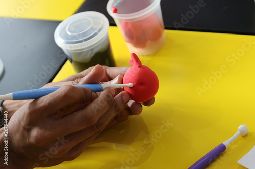 red play dough is decorated by hand and plastic sculpture tool on yellow table