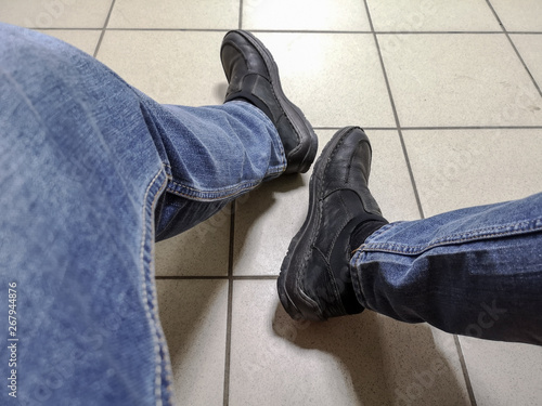 Men's feet in jeans and shoes on the tile
