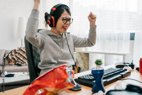 Professional gamer girl putting on headset and starts playing online video game on personal computer. Casual asian geek woman. happy female in eyeglasses winning pc game at home with yes hand gesture photo