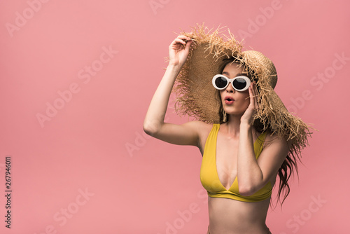 surprised girl in straw hat and sunglasses isolated on pink