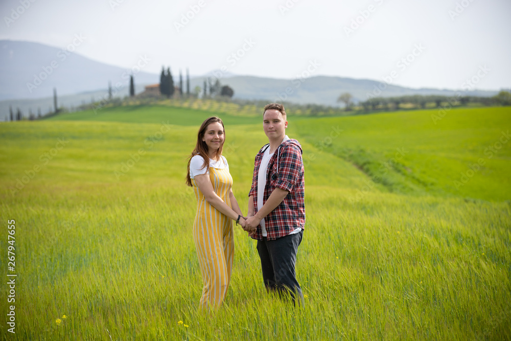 A young happy couple standing on a green meadow holding hands