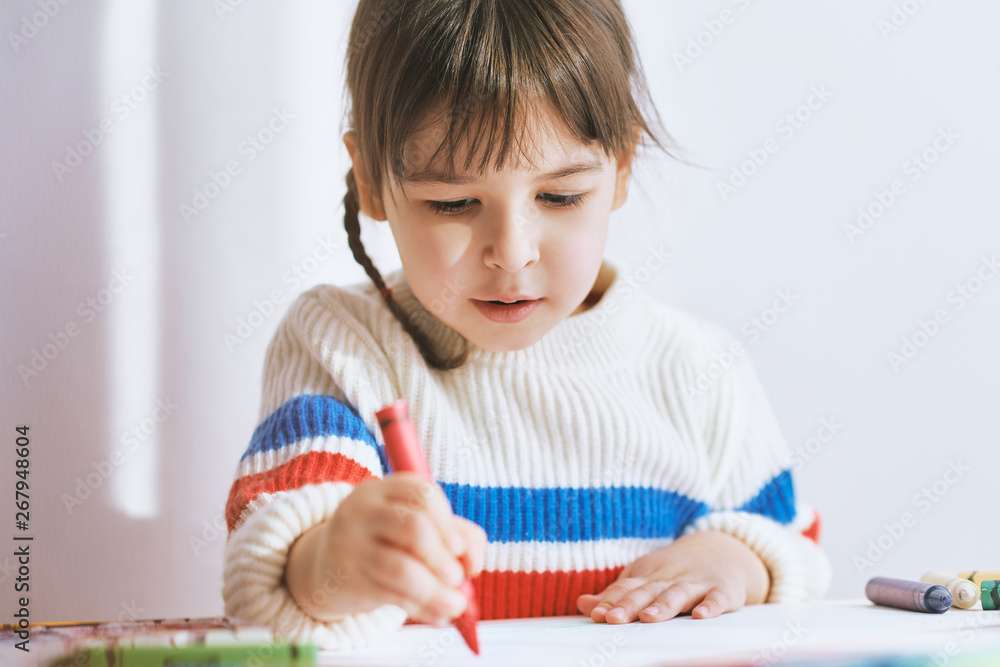 Creative little girl painting with colorful pencils, sitting at white desk at home. Joyful child drawing with pencils. People, childhood and education concept Creative little girl painting with colorful pencils, sitting at white desk at home. Joyful child drawing with pencils. People, childhood and education concept