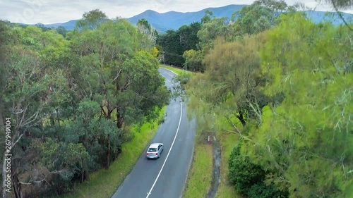 Slow aerial rise over cars driving on rural road revealing scenic countryside and mountains in Healesville, Victoria, Australia