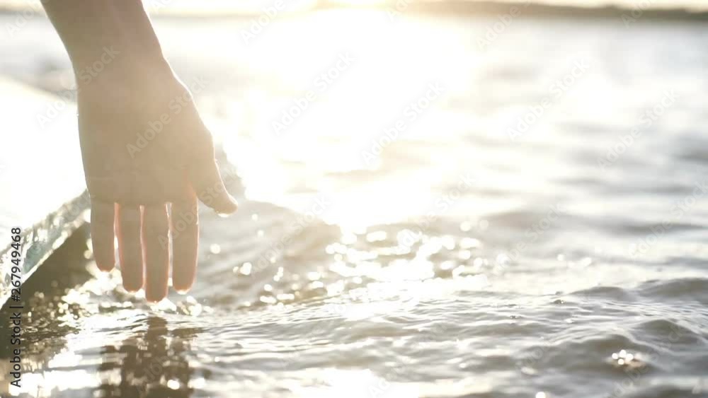 At sunset, close-up the hand of a girl moving through the water At sunset, close-up the hand of a girl moving through the water