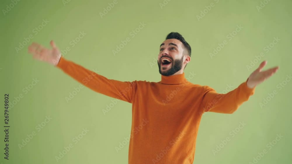 Handsome bearded young guy laughing raising arms looking at camera on green background celebrating success and rejoicing. Happy people and success concept. Handsome bearded young guy laughing raising arms looking at camera on green background celebrating success and rejoicing. Happy people and success concept.
