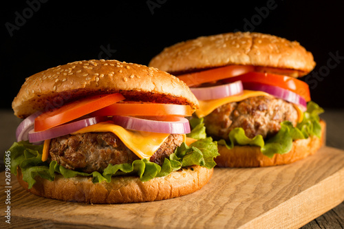 Home made hamburger with beef, onion, tomato, lettuce and cheese. Fresh burger close up on wooden rustic table with potato fries, beer and chips. Cheeseburger.