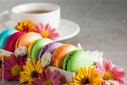 Still life and food photo of cake macarons in a gift box with flowers, a cup of tea on light background. Sweets and desserts concept of macaroons.